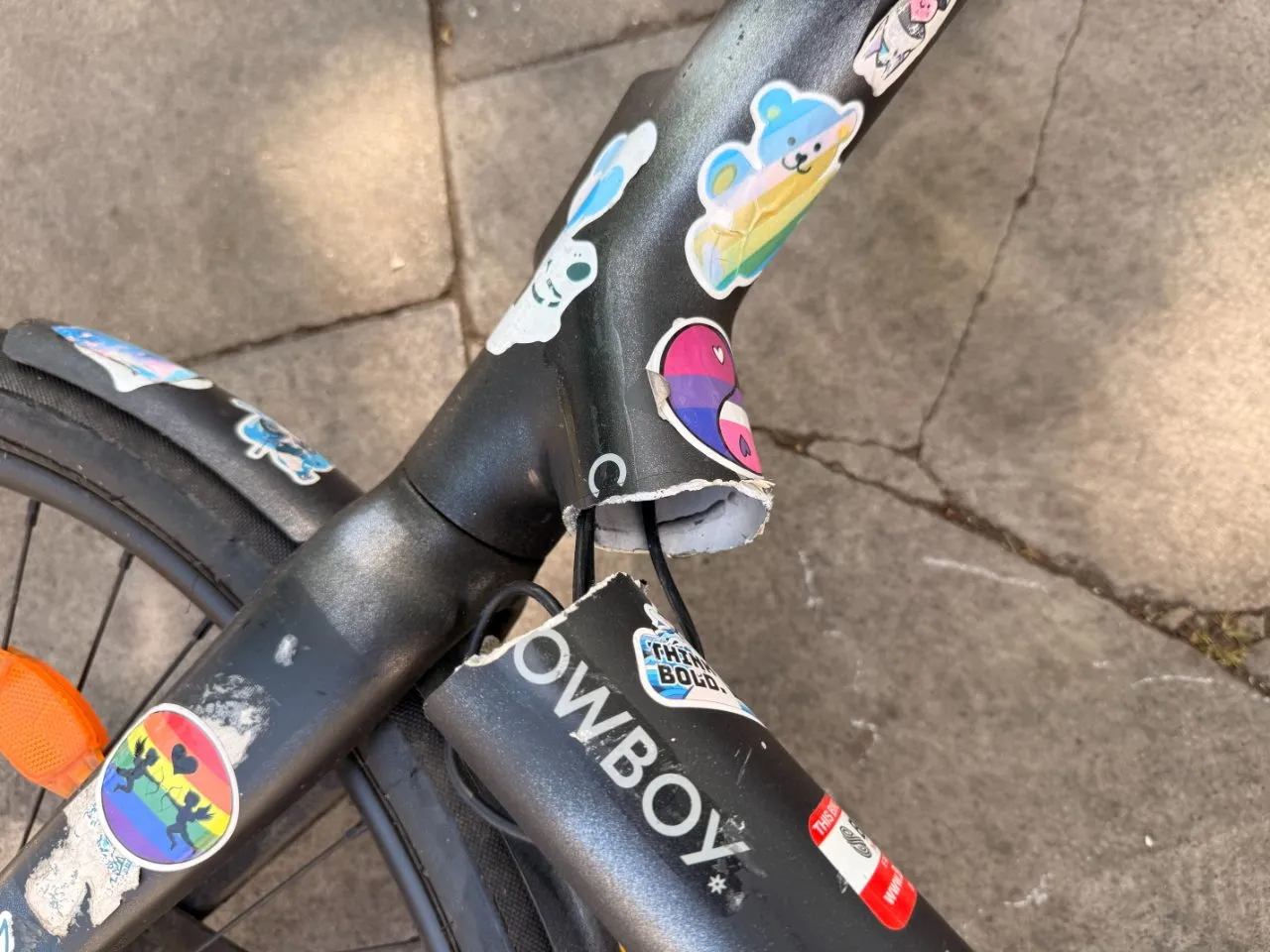 A Cowboy C4 ST frame sheared clean through at the headtube joint, the COWBOY wordmark visible just below the break, on a London street.